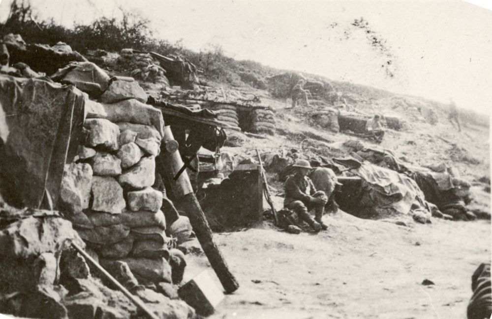 Dugouts on what appears to be a rail embankment. The marked shell sitting on a log is used as a gas alarm. 1916.